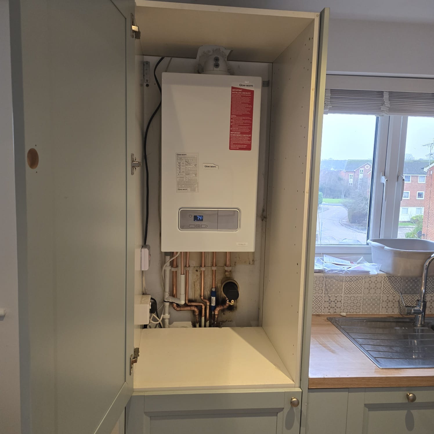 Glow-worm boiler installed inside a kitchen cupboard beside a window in an Essex home