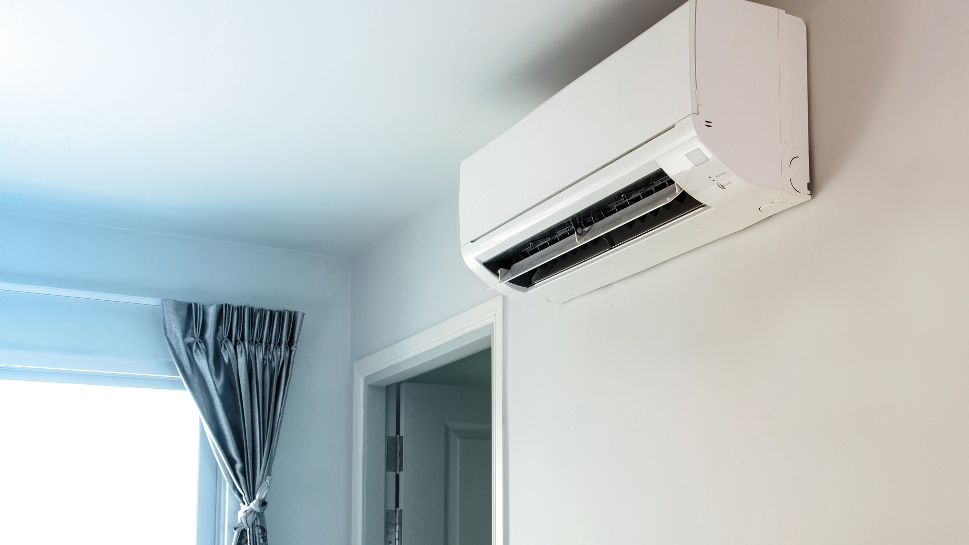Wall-mounted air conditioning indoor unit installed above a doorway in a bright Essex home